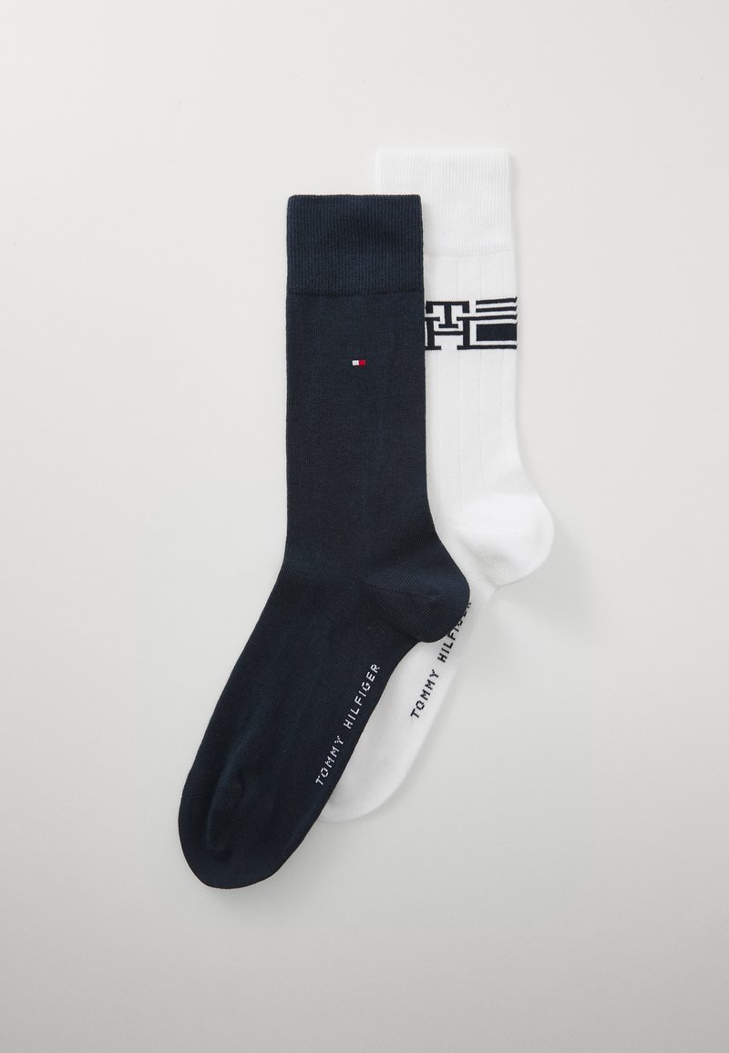 Deux paires de chaussettes : une paire navy avec un petit logo et une chaussette blanche comportant des rayures horizontales sombres et le nom de la marque au bas.