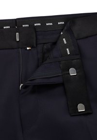 Marineblaues Hosen mit Reißverschluss, ausgestattet mit einem Haken- und Ösenverschluss. Enthält einen schwarzen Bund mit wiederholtem "BOSS"-Branding.