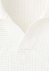 Gros plan sur un tissu blanc texturé avec un détail de col plié ressemblant à un motif de tricot gaufré.