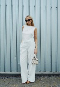 White sleeveless top and wide-leg pants outfit, featuring a structured design. Accessories include a small handbag and pointed heels. Black sunglasses.