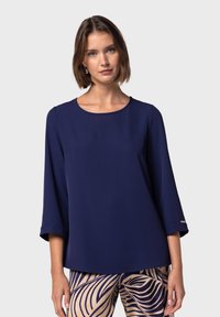Top blu navy in tessuto leggero con scollatura rotonda e maniche a tre quarti; presenta un dettaglio argentato all'orlo della manica.