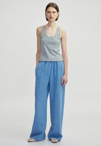 Grijze gebreide tanktop met een ronde hals, gecombineerd met losse blauwe denim broek met gouden bloemenborduursel en zijzakken.