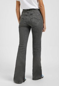 Jeans acampanados de color gris oscuro con una cintura alta, que presentan bolsillos traseros, costuras en contraste y una ligera textura vintage.