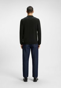 Maglietta nera a maniche lunghe con colletto, abbinata a jeans blu scuro, larghi e a scarpe nere. Design semplice e minimal.