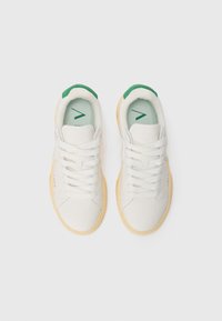 White sneakers with green accents, textured upper, round toe, and chunky rubber sole. Features lace-up design and subtle branding on side.