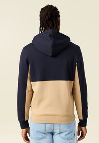 Felpa con cappuccio caratterizzata da una parte superiore blu navy e una parte inferiore beige, realizzata in tessuto morbido, con polsini a coste e un design dalla vestibilità rilassata.