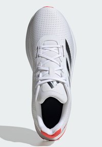 Zapatilla deportiva blanca con parte superior de malla, acentos negros y una pestaña trasera rosa. Las características incluyen cordones, una lengüeta acolchada y detalles texturizados.