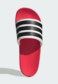 Sorte og hvide slidesandaler med tre horisontale striber på en struktureret rem, rød sål og logo-detalje prægede på sålen.