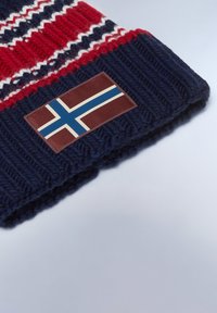 Beanie lavorato a maglia in blu navy con fascette rosse e bianche, dotato di una toppa rettangolare che mostra la bandiera islandese. Materiale in morbida lana.