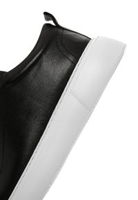 Sneaker in pelle nera con texture liscia, suola in gomma bianca e cuciture a contrasto. Presenta un'etichetta sul tallone per una facile calzata.