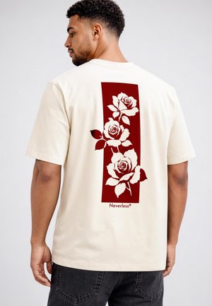 Man wearing a cream t-shirt with a large maroon rectangular print of three white roses on the back and the word "Neverless" below.