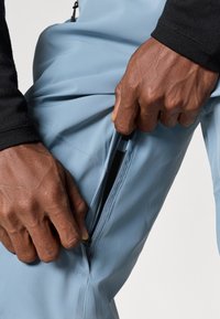 Kék sportnadrág oldalzippel, könnyű, sima anyagból készült. Közeli felvétel a zippert fogó kezekről, a könnyű hozzáférhetőség érdekében.