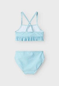 Šviesiai mėlynas dryžuotas bikini komplektas su volanų viršumi, kryžminėmis petnešomis ir paprastomis kelnaitėmis su elastine juosta. Minkšta audinio tekstūra.