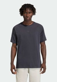 Tmavomodré tričko s krátkym rukávom a okrúhlym výstrihom, s jemným logom na hrudi a raglánovými rukávmi, vyrobené z ľahkej látky.