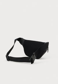 Zwarte schoudertas met een geëtst mesh lichaam, gebogen vorm, verstelbare riem en plastic gesp sluiting. Voorzien van een onopvallend ritssluitingvak.