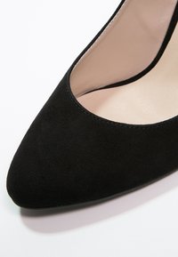 Chaussure à talon haut en daim noir avec un bout pointu et un design de tige basse, présentant une doublure intérieure lisse et des coutures visibles minimales.