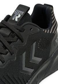 Zwarte sportieve schoen met een bovenkant van gestructureerde stof, contrasterende grijze accenten en een rubberen zool. Heeft een logo op de tong en gestreepte details.