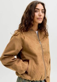 Brun ruskind bomberjakke med lynlås foran, ribbet krave og sidelommer, der har en blød tekstur og en løs pasform.