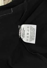 Mustikka puuvillakangas, jossa on hoito-ohjeita näyttävä care label, materiaalitiedot ja symbolit pesunhoidolle. Teksti useilla kielillä.
