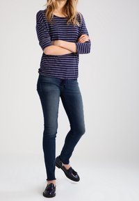 Top de manga larga a rayas marinas, hecho de una tela texturizada. Combinado con jeans skinny azul oscuro y mocasines negros brillantes. Atuendo casual.