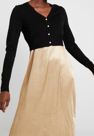 Abito lungo con parte superiore nera a maglia con bottoni e scollatura a V, che si trasforma in una gonna liscia di un leggero beige simile alla seta.
