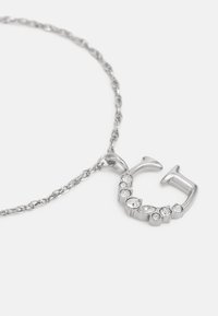 Colar de corrente em prata com um pendente em forma de ‘C’ adornado com várias pedras transparentes em diferentes formas e tamanhos.
