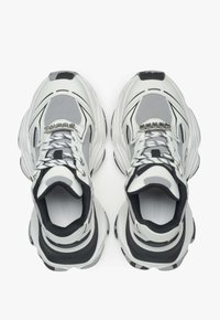 Witte en zwarte sportschoenen met een bovenwerk van mesh, een stevige zool en een opvallend vetersysteem. Kenmerkt zich door slanke lijnen en minimalistische designelementen.