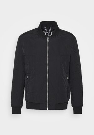Veste bomber noire avec texture matelassée, poignets et ourlet côtelés, fermeture éclair sur le devant, et détails de branding ton sur ton subtil sur le tissu.