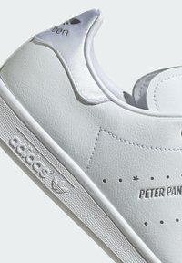 White sneakers with a textured leather upper, satin accents, perforated details, and embossed branding on the side. Thick rubber sole.