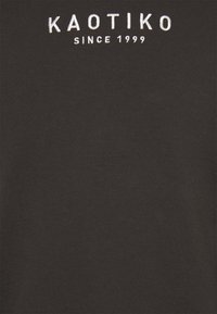 T-shirt in cotone nero con ricamo bianco con la scritta "KAOTIKO" e "SINCE 1999" sul davanti. Collo a giro e maniche corte. Texture liscia.