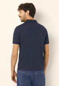 Marinblå pikétröja med korta ärmar och krage, tillverkad av ett slätt tyg. Matchas med denimshorts med bakfickor.