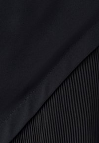 Gros plan sur un tissu noir montrant une section lisse chevauchant une section à texture côtelée verticale avec des coutures visibles.