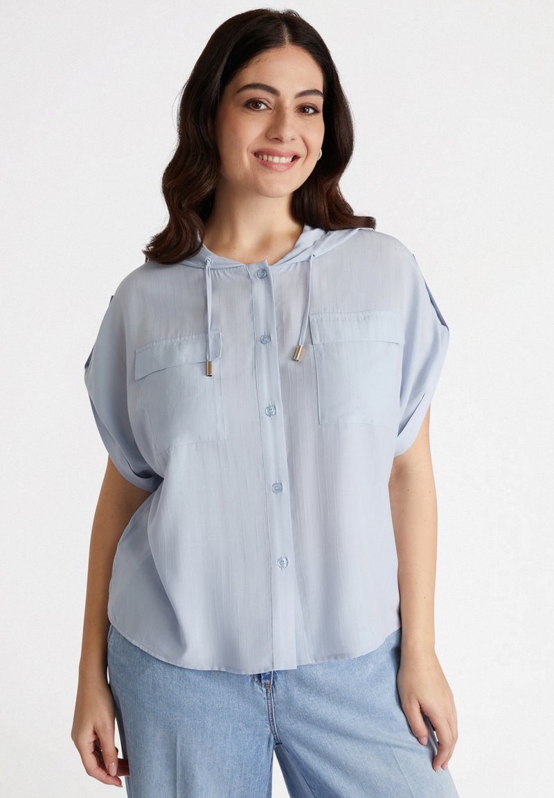 Camicia a maniche corte azzurro chiaro con cappuccio, dotata di due tasche sul petto e chiusura frontale con bottoni. Realizzata in un tessuto trasparente e texture.