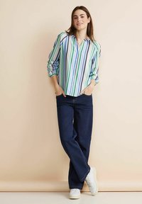 Randig skjorta i blått, grönt och vitt, med långa ärmar och avslappnad passform, tillsammans med mörkblå jeans och vita sneakers.