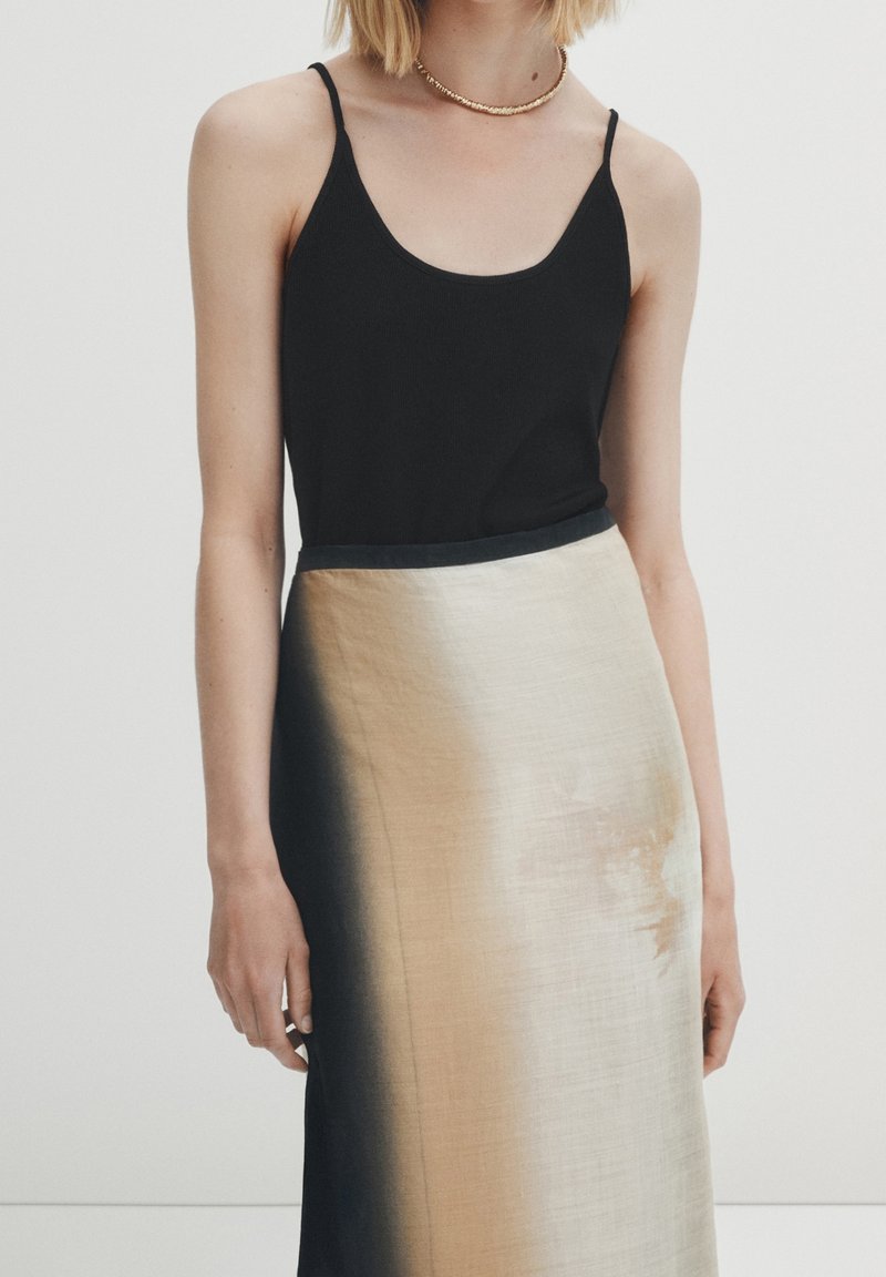 Top nero con spalline sottili abbinato a una gonna in satin beige e nera con gradiente, caratterizzata da una texture liscia e una leggera lucentezza.