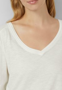 Witte V-hals top gemaakt van lichte, getextureerde stof. Heeft een subtiel gemêleerd patroon en een comfortabele, ontspannen pasvorm.