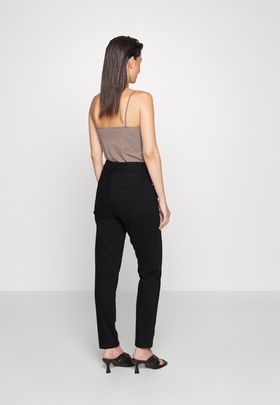 Pantalones negros de cintura alta con un ajuste recto, con textura de mezclilla y bolsillos traseros. La modelo lleva una camiseta sin mangas ajustada de color marrón claro.