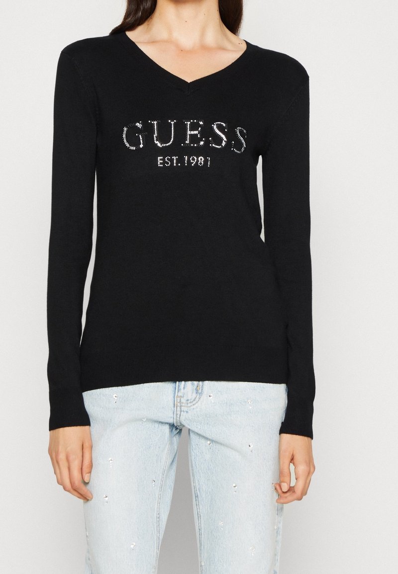 Zwarte lange mouwen trui met V-hals, met zilveren rhinestone merknaam "GUESS EST. 1981" aan de voorkant, geribde manchetten en zoom.