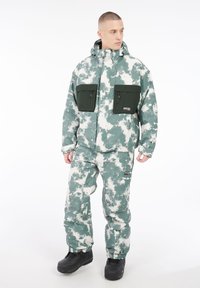 Winterjacke und Hose im grün-weißen Camouflage-Muster. Die Jacke verfügt über zwei große Reißverschlusstaschen und eine Kapuze. Robustes Material, lockere Passform.