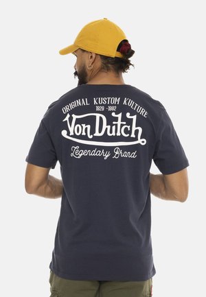 Un t-shirt en coton bleu marine avec du texte imprimé blanc au dos, incluant "Von Dutch" et "Legendary Brand", avec une coupe décontractée.