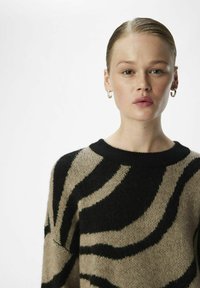 Pull beige avec un imprimé animal noir audacieux, encolure ronde, texture douce et coupe ample. Accentué par des poignets et un ourlet côtelés.