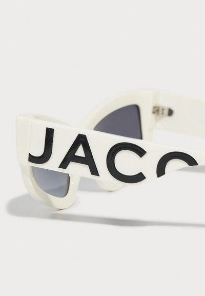 White sunglasses with oversized black lettering spelling "JACO" on the side. Dark tinted lenses and a sleek, modern design.