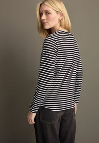 Schwarz-weißer gestreifter Langarm-Oberteil mit rundem Halsausschnitt, kombiniert mit dunklen, hoch taillierten Jeans. Glattes Material und taillierte Passform.