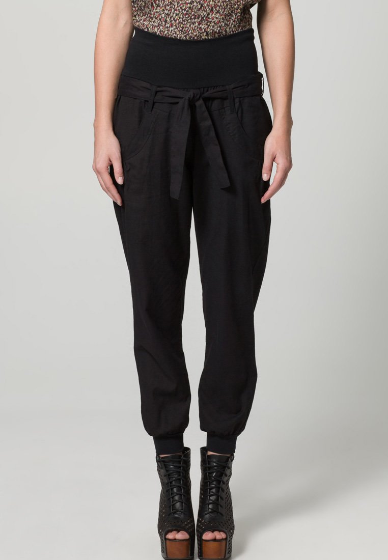 Pantalones jogger negros de cintura alta con detalles de lazo, que cuentan con bolsillos laterales y un corte relajado, combinados con zapatos de plataforma negros con cordones.