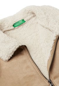 Giacca marrone in faux suede con fodera in sherpa color crema. Presenta una chiusura con cerniera e un'etichetta "United Colors of Benetton" all'interno del colletto.