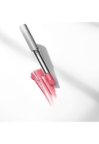 Rouge à lèvres avec un tube métallique argenté et un bâton rose, accompagné d'échantillons de couleur rose sur une surface blanche. Texture lisse, design moderne.