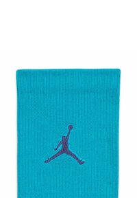 Calza sportiva turchese con texture a coste, con il logo Jumpman viola ben visibile nella parte anteriore.