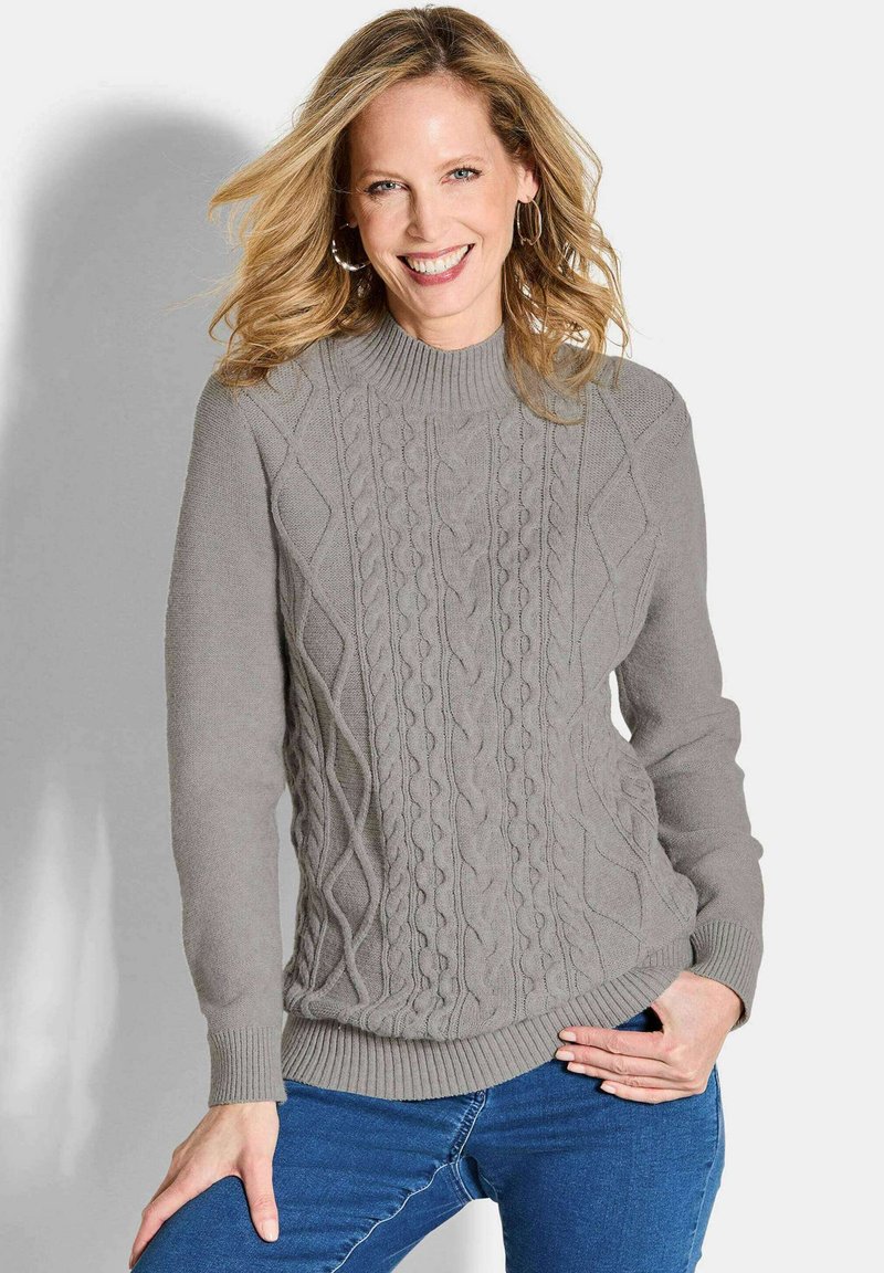 Grau gestrickter Pullover mit strukturiertem Zopfmuster, gerippten Bündchen und Saum. Kombiniert mit blauen Jeans, lässig getragen.
