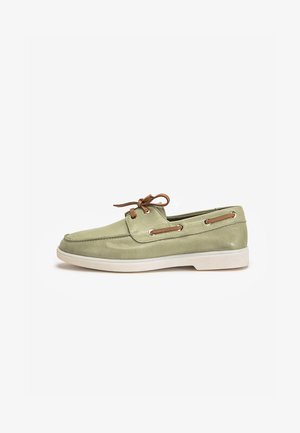 Chaussure bateau en daim vert avec lacets en cuir beige, œillets métalliques et semelle en caoutchouc blanche. Dispose d'un bout rond et d'éléments de design classiques.