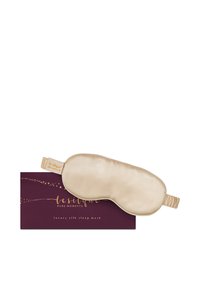 Beige Seidenschlafmaske mit elastischem Band, die auf einer dunkelvioletten Schachtel mit dem Aufdruck "le silque pure moments luxury silk sleep mask." liegt